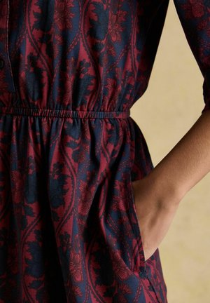 Floral print dress in navy and burgundy, featuring an elastic waistband and side pockets. Soft fabric with subtle texture. Button closure at the top.