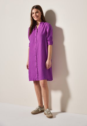 Robe en lin violet avec un devant à boutons, des manches roulées et un col, associée à des chaussures de sport beiges sur un fond clair.