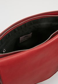 Červená kožená kabelka částečně otevřená, ukazující černou látkovou podšívku s kapsou na zip a štítkem značky Anna Field uvnitř.