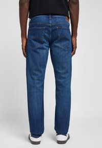 Temno modri jeans z ravnim krojem, ki imajo dva zadnja žepa in izrazito šivano šivko. Teksturni material z rahlim sijajem.