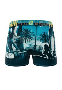 Shorts de baignade pour hommes avec un design bleu orné de graphismes de skateboard, de palmiers et d'une ceinture élastique jaune portée avec le texte "GUNFREE".