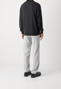 Dunkelgrauer gestrickter Pullover mit gerippten Bündchen und Saum, kombiniert mit hellgrauen Hosen und schwarzen Schuhen, von hinten betrachtet.