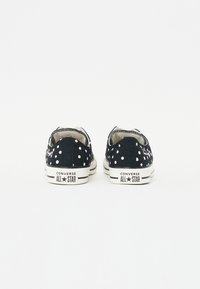 Fekete vászon tornacipők fehér pöttyökkel, gumitalppal, fűzős zárással és "Converse All Star" felirattal a saroknál.
