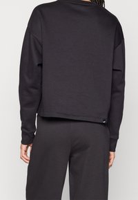 Sweatshirt noire raccourcie en tissu doux. Présente une conception à épaules tombantes, un col côtelé et une petite étiquette logo à l'ourlet.