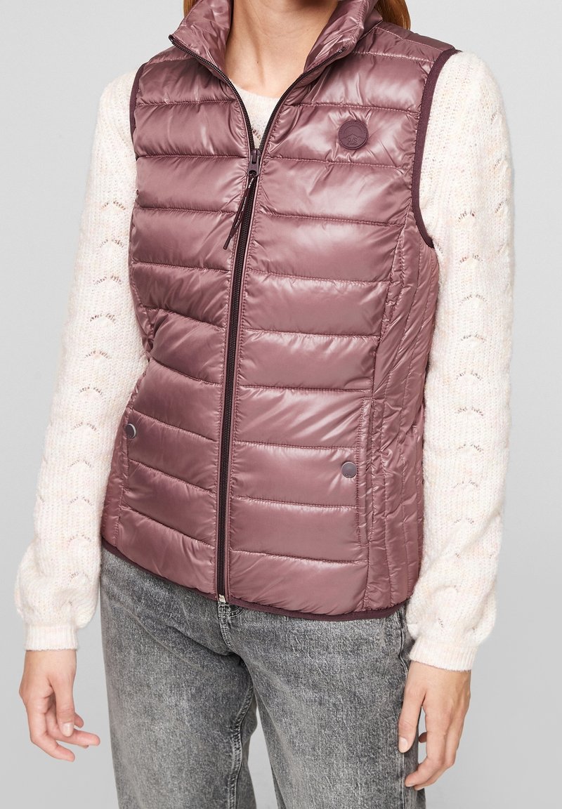 Chaleco ligero sin mangas en color malva, con diseño acolchado, cuello alto y cierre frontal con cremallera. Acentuado con botones de presión en el dobladillo.