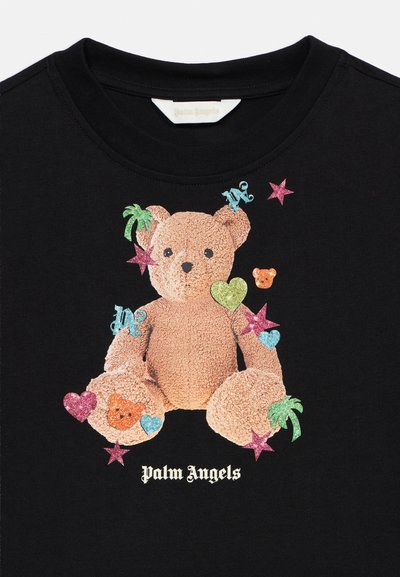 Εικονογράφηση λούτρινου αρκούδου με πολύχρωμα αστέρια, καρδιές, φοίνικες και γράμματα σε μαύρο ύφασμα, με το κείμενο «Palm Angels» από κάτω.