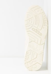 Semelle de sneaker blanche avec des motifs texturés et un logo. Présente des rainures pour l'adhérence et un design de orteil lisse et arrondi.