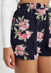 Námořnické květinové šortky s elastickým staženým pasem, zdobené růžovými a zelenými botanickými potisky na hladké tkanině.