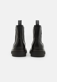 Bottes basses en cuir noir à finition lisse, avec des panneaux élastiques sur les côtés et des languettes à l'arrière. Semelles épaisses en caoutchouc avec détails de crampons.