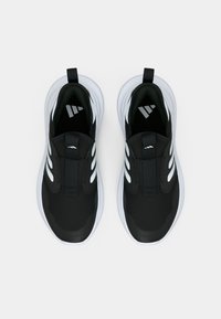 Scarpe da ginnastica nere senza lacci con strisce curve bianche sui lati e suole spesse bianche, viste dall'alto su uno sfondo bianco uniforme.