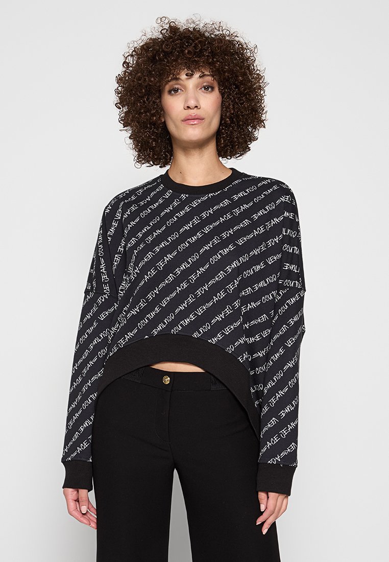 Sudadera de pulóver en negro con un patrón de texto en blanco repetido. Tiene un escote redondo, hombros caídos y puños acanalados. Material de mezcla de algodón.