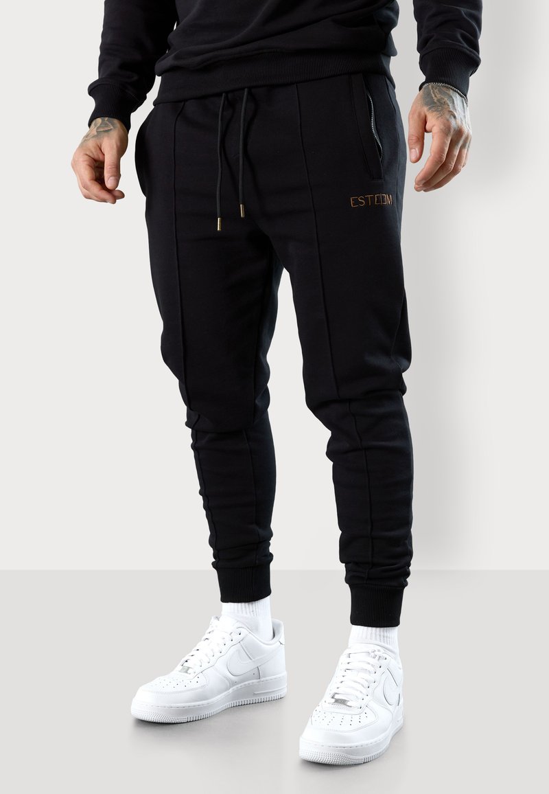 Schwarze Jogginghose mit elastischem Bund und Kordelzug, ausgestattet mit Seitentaschen und einem strukturierten Design. "ESTD"-Logo in Gold.