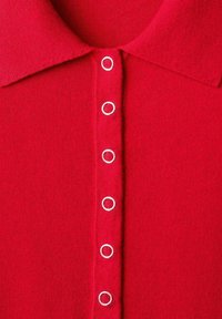 Polo en tricot rouge avec un col classique et six boutons métalliques blancs à ouvertures circulaires le long de la patte de boutonnage. Texture douce.