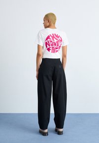 Hvit bomulls T-skjorte med stor rosa sirkulær grafisk tekst som sier "THE NORTH FACE" på baksiden. Sammen med løse, svarte bukser og sandaler.