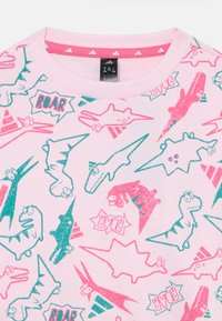 Sweat-shirt rose avec un motif graphique répété de dinosaures et "ROAR" en teal et rouge. Tissu doux avec un col rond et des poignets côtelés.