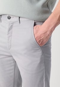 Jasnoszare chinosy o gładkiej fakturze, z przednią kieszenią i zapięciem na guzik. Widoczne przeszycia i klasyczny krój. Noszone z jasną zieloną bluzką.