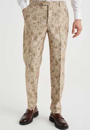 Beige bukser med brunt blomsterprint, presfolder foran, båret med hvid skjorte og mørkebrune læder loafers.