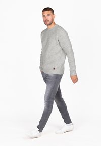 Lichtgrijze geribbelde trui met een ronde halslijn, gedragen met vervaagde grijze spijkerbroek en witte sneakers, met een klein label op de trui.