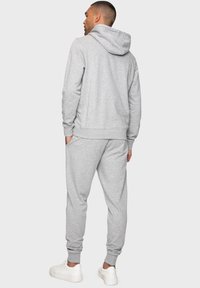 Grijze hoodie en joggers, gemaakt van zachte stof, met een regular fit. Voorzien van ribgebreide manchetten en zoom. Witte sneakers maken de outfit compleet.