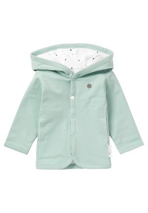 Veste bébé vert clair avec capuche doublée en tissu blanc à étoiles noires, boutons-pression à l'avant et petit logo trèfle sur la poitrine.