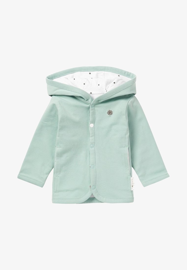 Veste bébé vert clair avec capuche doublée en tissu blanc à étoiles noires, boutons-pression à l'avant et petit logo trèfle sur la poitrine.