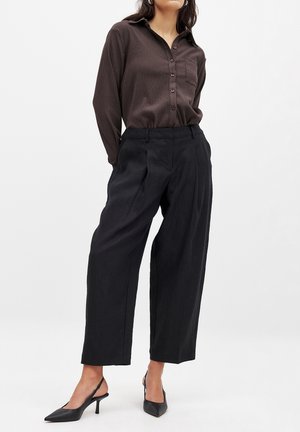 Bruine button-up shirt met een gestructureerde afwerking, gecombineerd met hoge, zwarte wijde broek en zwarte slingback hakken.
