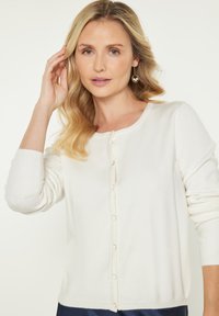 Ivoor gebreide cardigan, zachte textuur, ronde halslijn, lange mouwen, sluiting met knopen aan de voorkant met kleine ronde knopen, minimalistisch ontwerp.