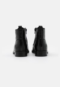 Svarta läderankelstövlar med slät finish, sidodragkedjor och en liten ögla baktill för enkel påtagning. Låga, stadiga klackar.