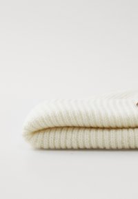 Soft, folded cream-colored knit sweater with ribbed texture against a plain white background.
