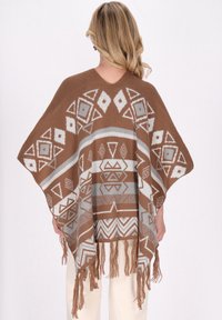 Braun gemusterter Poncho mit geometrischen Designs in Creme und Grau, mit Fransen am Saum und einem entspannten, offenen Schnitt.