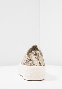 Sneaker Converse All Star a basso profilo con pattern in serpente beige e marrone vista da dietro su una superficie e sfondo bianchi.