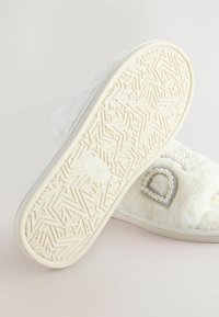 White, fluffy slipper with a textured sole featuring star patterns. Decorated with a pearl-embellished heart accent. Size marked "M."