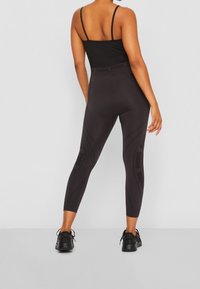 Czarna bluzka sportowa z cienkimi ramiączkami oraz wysokim stanem, dopasowane czarne legginsy z teksturowanymi detalami po bokach i logo na pasku.