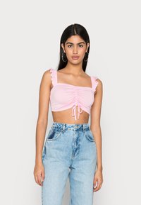 Top cropped rosa com alças franzidas, detalhes reunidos no centro e um laço na bainha; combinado com jeans de cintura alta azul claro.
