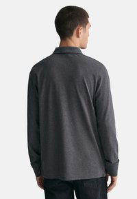 Herren Langarmhemd in Dunkelgrau, aus weichem Stoff gefertigt. Mit einem klassischen Kragen, Seitenschlitzen und Knopfmanschetten.