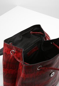 Punainen käärmeenahkakuosinen olkalaukku, jossa musta kangasvuori, yläosassa nyöri ja hopeanväriset metalliosat. Sisältää vetoketjullisen sisätaskun.