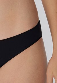 Schwarze Bikiniunterteile mit nahtlosem Design, das eine glatte Textur und eine niedrige Passform bietet. Der Stoff wirkt dehnbar und leicht.