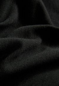 Tissu noir à côtes avec une surface texturée, présentant de grandes lignes horizontales et des plis doux, créant une apparence ondulée.