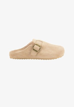 Zapato beige de ante tipo slip-on con punta redondeada, correa lateral con hebilla y suela texturizada para mayor adherencia. Material suave con acabado liso y diseño minimalista.