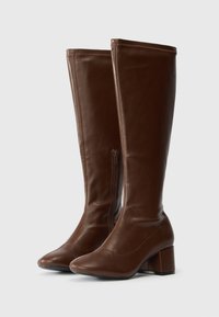 Brown leather knee-high boots with a pointed toe, block heel, smooth texture, and a side zipper detail.