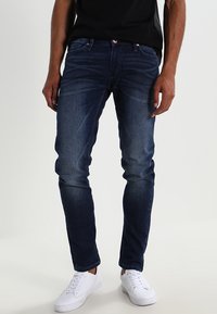 Mörkblå denimjeans med slim fit, med framfickor, knäppning och synliga sömmar. Tillsammans med vita sneakers.