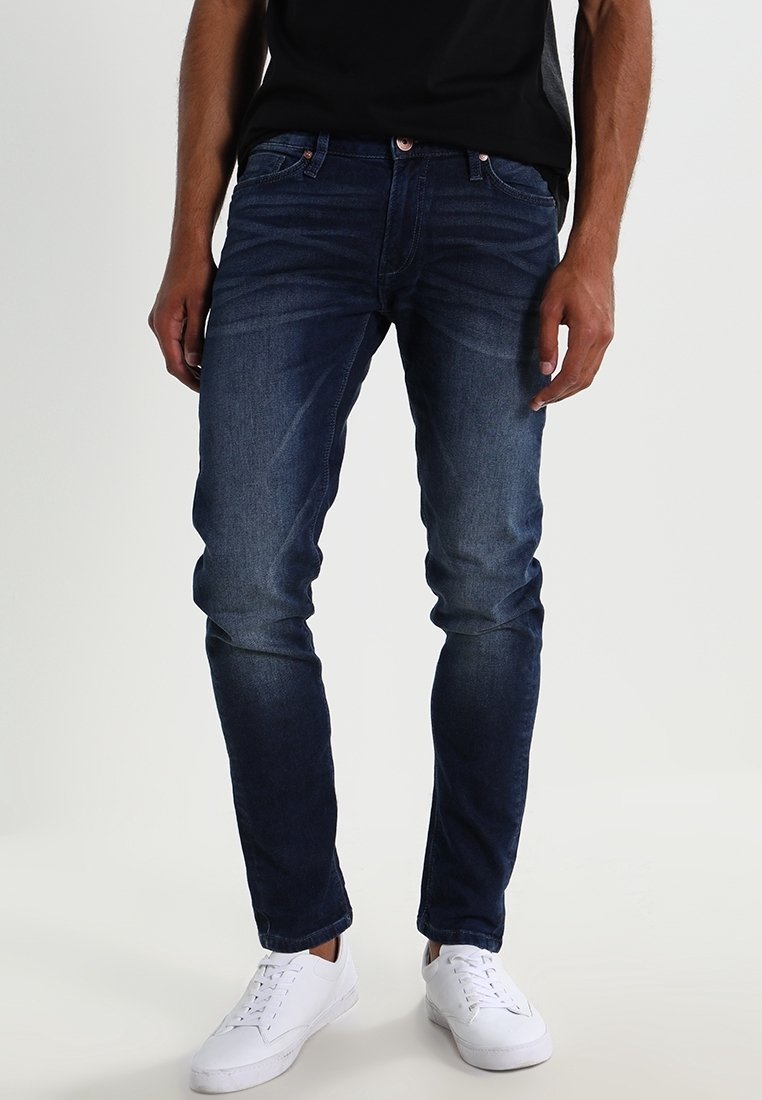 Mörkblå denimjeans med slim fit, med framfickor, knäppning och synliga sömmar. Tillsammans med vita sneakers.