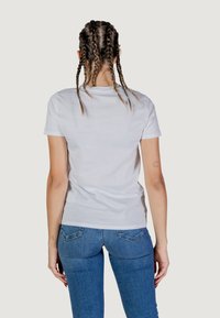 T-shirt bianca in cotone con maniche corte, scollo rotondo e vestibilità aderente. Indossata con jeans in denim blu, vista da dietro.