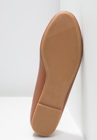 Chaussure plate marron avec semelle en caoutchouc texturée, indiquant la taille 38 et le nom de la marque sur la semelle, placée devant des murs blancs.