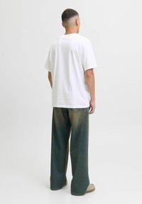 Bijela pamučna majica s kratkim rukavima, u kombinaciji s širokim izblijedjelim zelenim trapericama. Odjeća je upotpunjena bež obućom.