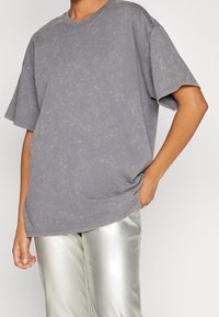 Šedé oversized tričko vyrobené z jemného materiálu, s jemným texturovaným vzorem a krátkými rukávy, doplněné lesklými stříbrnými kalhotami.