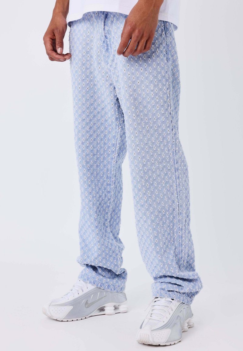 Pantalones deportivos azul claro con estampado, confeccionados en tela suave con una textura sutil; cuentan con cinturilla elástica y piernas ajustadas, combinados con zapatillas grises.