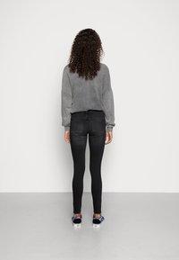 Camiseta gris de manga larga y holgada, jeans ajustados negros y zapatos de lona con estampado, vistos desde la parte de atrás sobre un fondo liso.