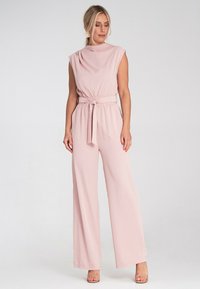 Różowy, bezrękawnikowy kombinezon z drapowaną szyją, w talii z paskiem i szerokimi nogawkami. Wykonany z gładkiego materiału, o luźnym kroju.