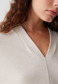 Beige, geripptes Stricktop mit V-Ausschnitt und figurbetontem Design, das eine weiche Textur und subtile vertikale Streifen betont.